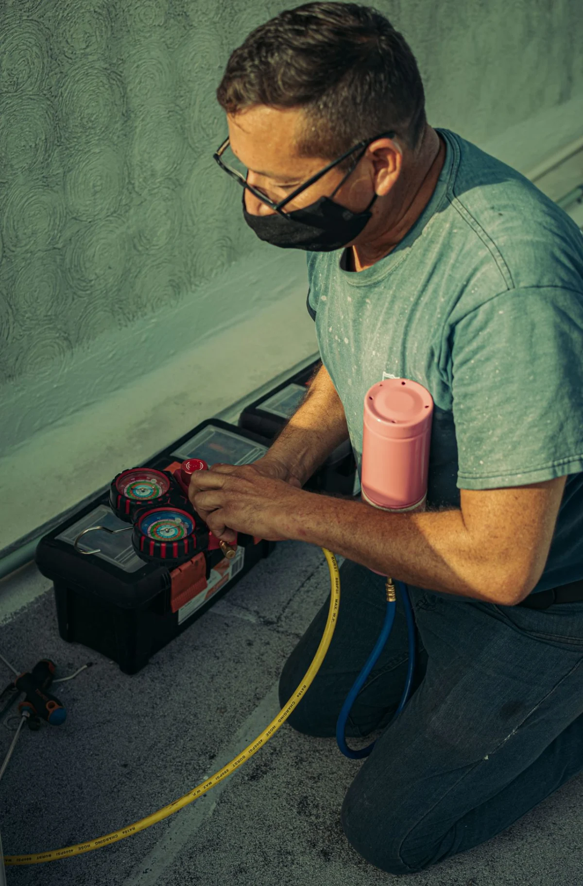 Technician kneeling to service an HVAC system with gauges